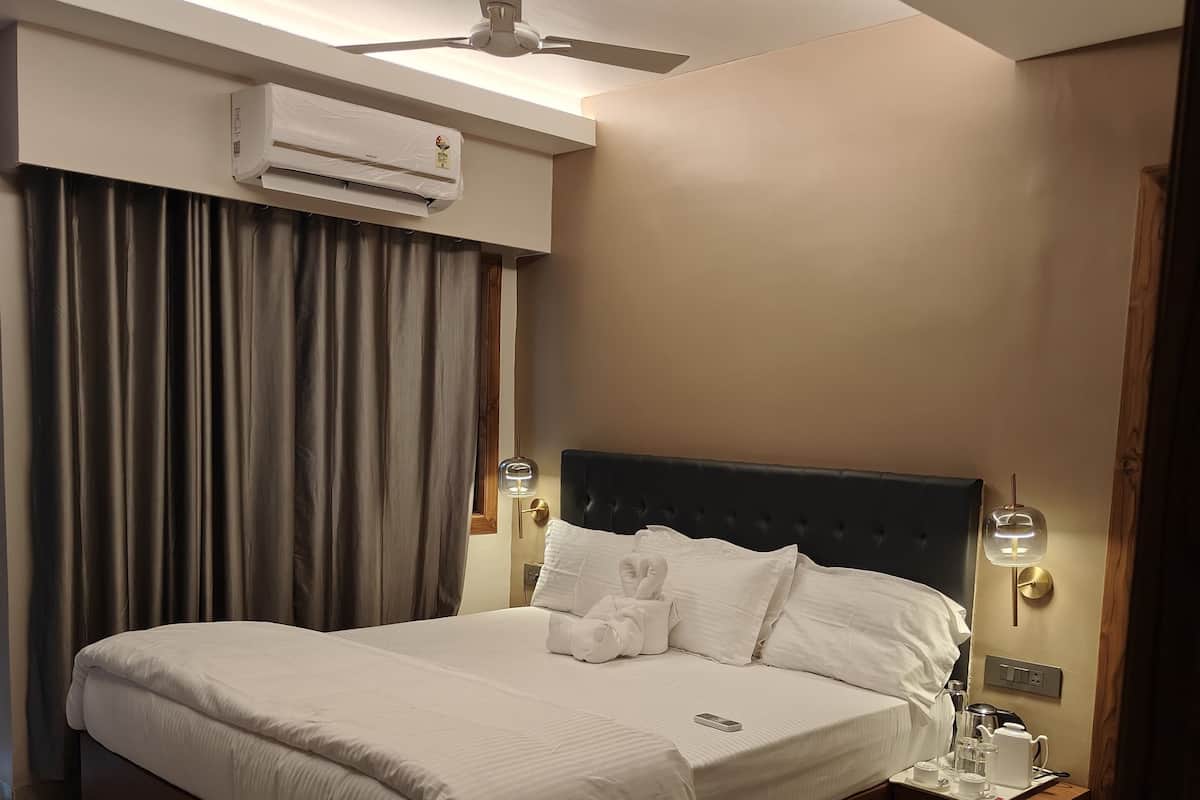 Una cama bien hecha con sábanas blancas, una mesita de noche con una lámpara y un ventilador de techo.