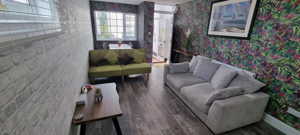 A living room with a green sofa, a grey sofa, a small table with a plant, and a window with bars. - The Hideaway ll /enclosed Garden/quiet/central (Southport)
