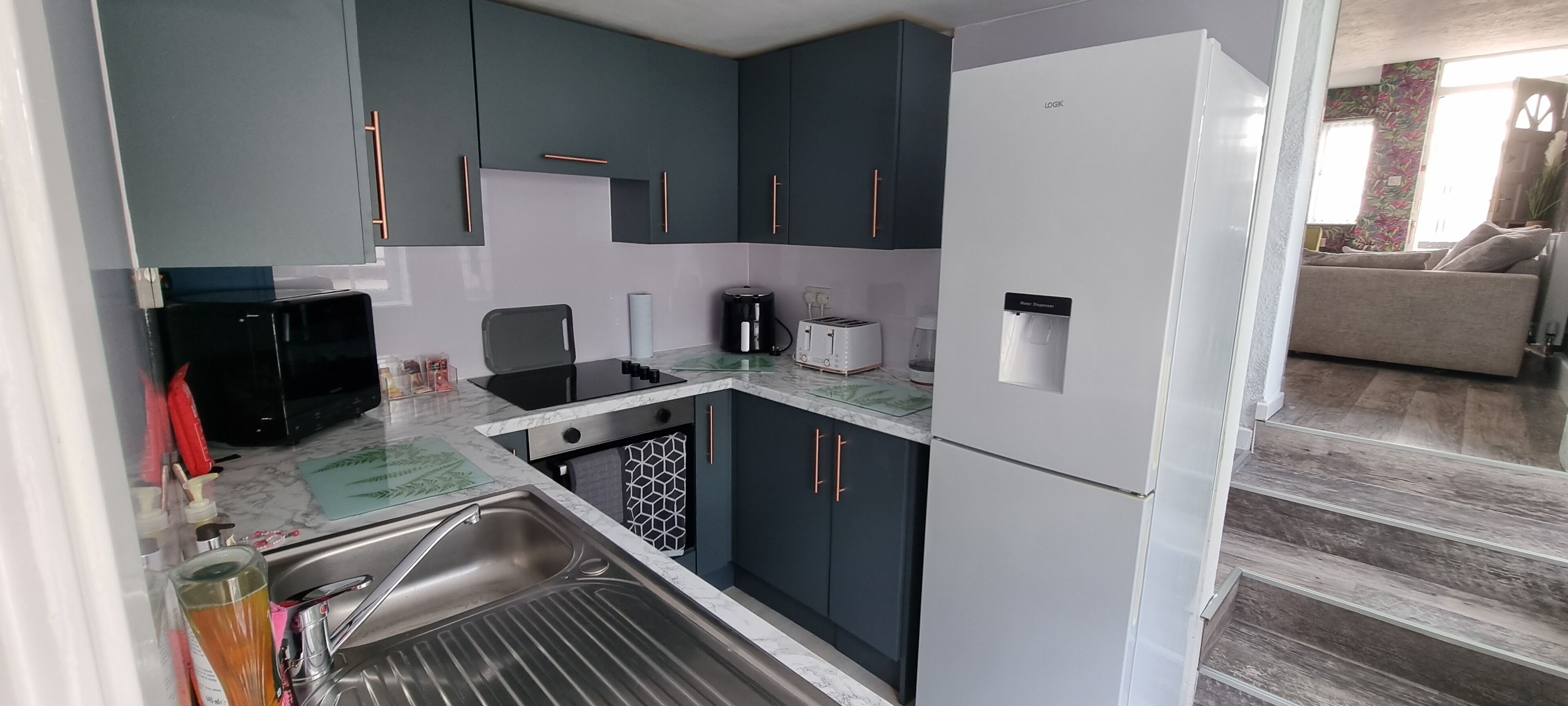 Eine kleine Küche mit dunklen Schränken, einem weißen Kühlschrank und einer Kaffeemaschine.