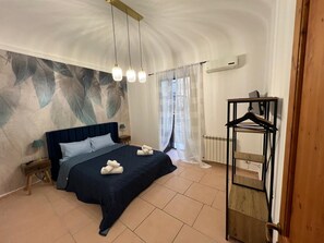 Een slaapkamer met een groot bed, een hanglamp, een radiator en een houten kledingrek.