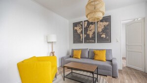 A living room with a sofa, a yellow chair, a coffee table, a lamp, and world maps on the wall. - TEA&CHILL - Mimosa - Proche métro 5 (Drancy)