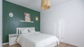 A bedroom with a white bed, green walls, a white nightstand, a decorative sign, and a woven light fixture. - TEA&CHILL - Mimosa - Proche métro 5 (Drancy)
