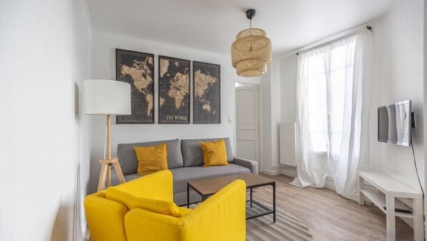 A modern living room with a sofa, yellow chairs, a coffee table, a lamp, a TV, and world maps on the wall. - TEA&CHILL - Mimosa - Proche métro 5 (Drancy)