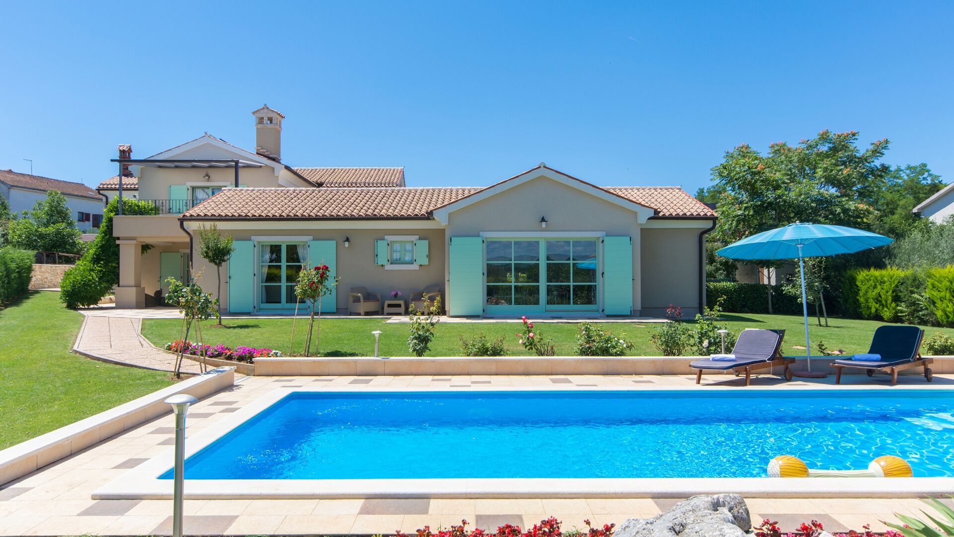 A two-story house with a swimming pool, a covered patio area, and a well-maintained garden.