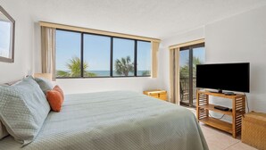 A bedroom with a large bed, a television on a wooden stand, and a view of the ocean through a large window. - ShorehamTowers Oceanfront Resort (NORTH MYRTLE BEACH)
