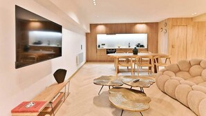 Ein modernes Wohnzimmer mit Fernseher, Esstisch aus Holz und einer Couch.