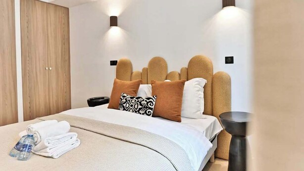 Une chambre d’hôtel moderne avec un grand lit, une armoire en bois et deux lampes fixées au mur.