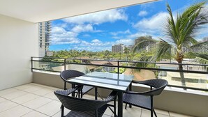 A balcony with a glass table and chairs, offering a view of palm trees and buildings.