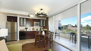 A modern kitchen with a dining area, a large sliding glass door leading to a balcony, and a view of palm trees.