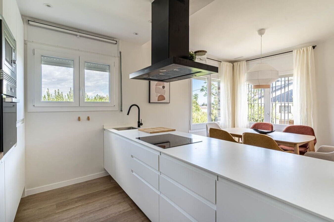 A modern kitchen with a large island, a built-in oven, and a window overlooking greenery.