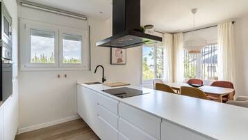 A modern kitchen with a large island, a built-in oven, and a window overlooking greenery.