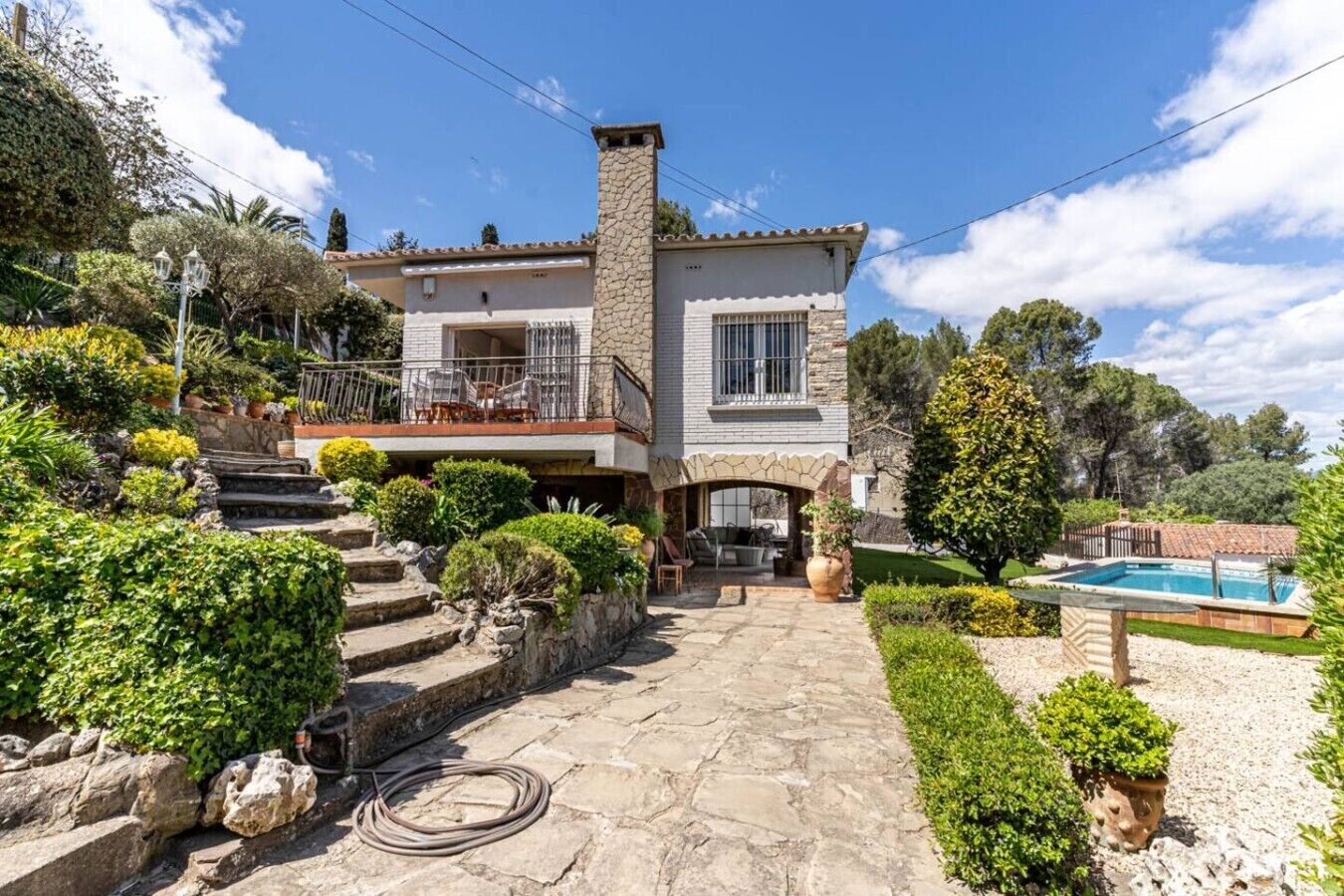 A two-story house with a stone facade, a balcony with outdoor furniture, and a swimming pool in the backyard.