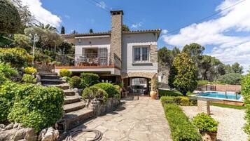 A two-story house with a stone facade, a balcony with outdoor furniture, and a swimming pool in the backyard.