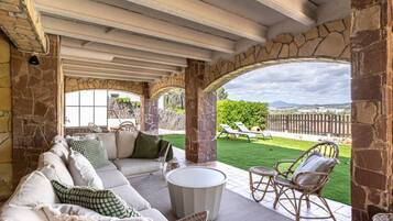 A covered outdoor seating area with a sofa and chairs, a table, and a view of a grassy yard.