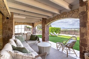 Ein überdachter Außenbereich mit einer Sitzecke, die eine Couch und Stühle sowie einen Tisch umfasst, mit Blick auf einen Rasen.