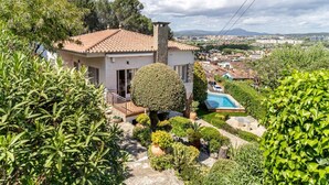A house with a red-tiled roof, surrounded by lush greenery, a swimming pool, and a view of a town in the distance. - Renovated villa, pool, barbecue, and just 15 minutes from Barcelona. (Sant Cugat del Vallès)