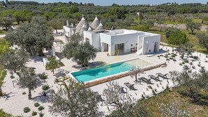 Una villa moderna con piscina, rodeada de olivos y un jardín paisajista.