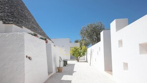 Un estrecho callejón con paredes blancas, un sendero de grava, un árbol y un banco.