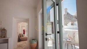 Una habitación con puerta de vidrio que da a un espacio exterior con mesa y sillas, una planta en maceta y un muro de piedra.