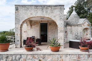 A stone building with an arched entrance, potted plants, outdoor furniture, and a view of the surrounding landscape. - Villa L Arco in Col by Wonderful Italy (Fasano)