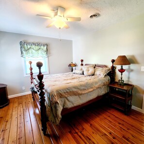 A bedroom with a wooden floor, a bed with a headboard, a ceiling fan, a window with a curtain, and a bedside table with a lamp. - Beautiful view from deck, Private Dock, Firepit, Golf Cart-items to the water. (Benton)