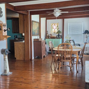 A wooden dining area with a table and chairs, a ceiling fan, and a kitchen in the background. - Beautiful view from deck, Private Dock, Firepit, Golf Cart-items to the water. (Benton)