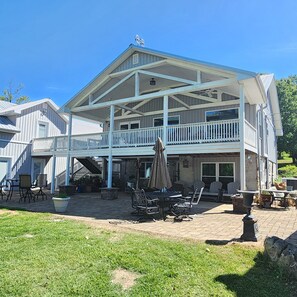A large, two-story building with a covered patio area, outdoor seating, and a staircase leading to the upper level. - Beautiful view from deck, Private Dock, Firepit, Golf Cart-items to the water. (Benton)