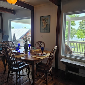 A dining area with a wooden table, chairs, and a view of a house and trees through a window.