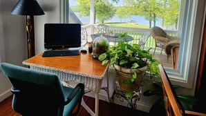 Ein Zimmer mit Schreibtisch, Laptop und Blick auf einen See und Bäume.