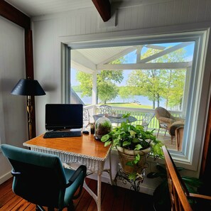 A room with a desk, laptop, and a view of a lake and trees.