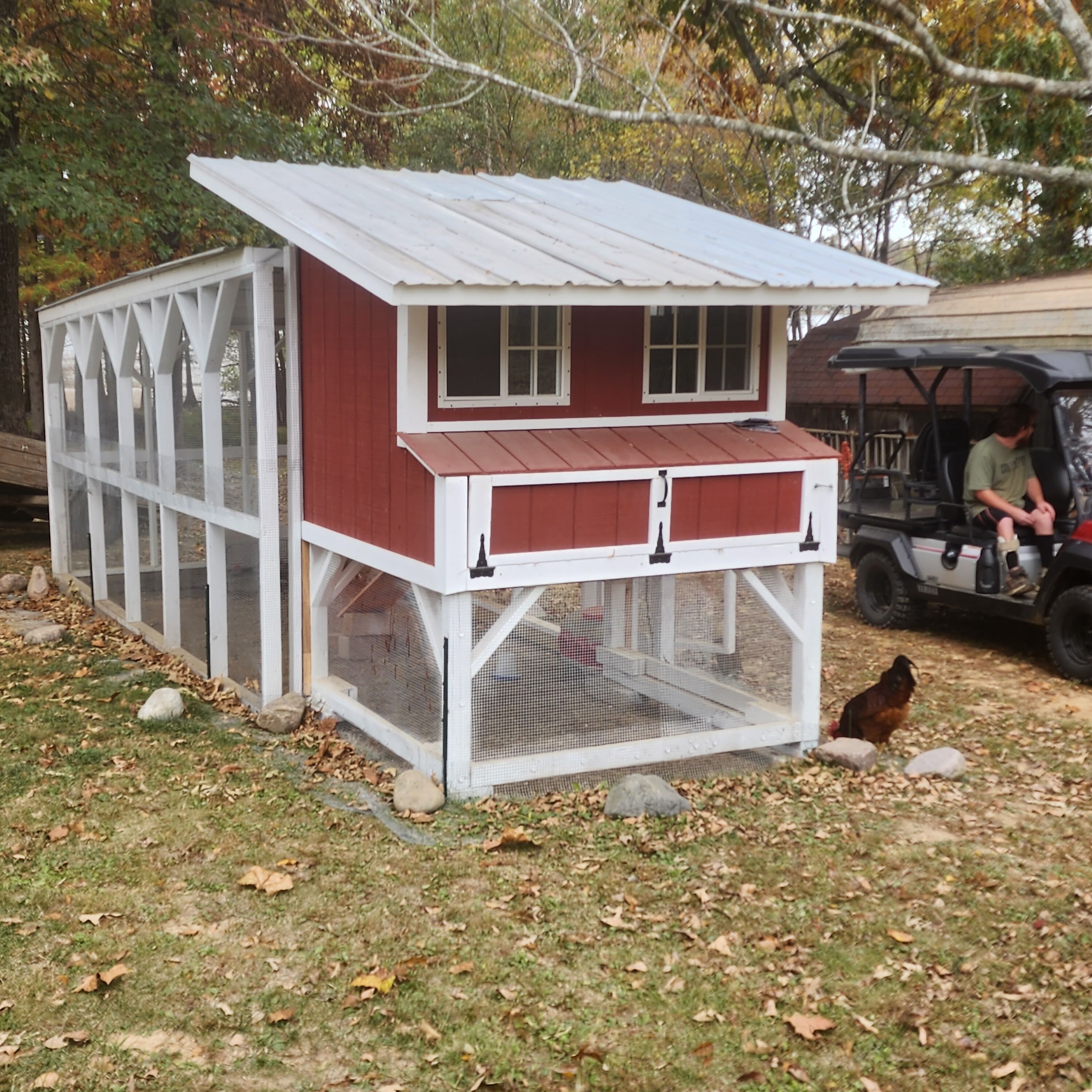 Un gallinero rojo y blanco con una zona cubierta para gallinas y un pequeño porche.