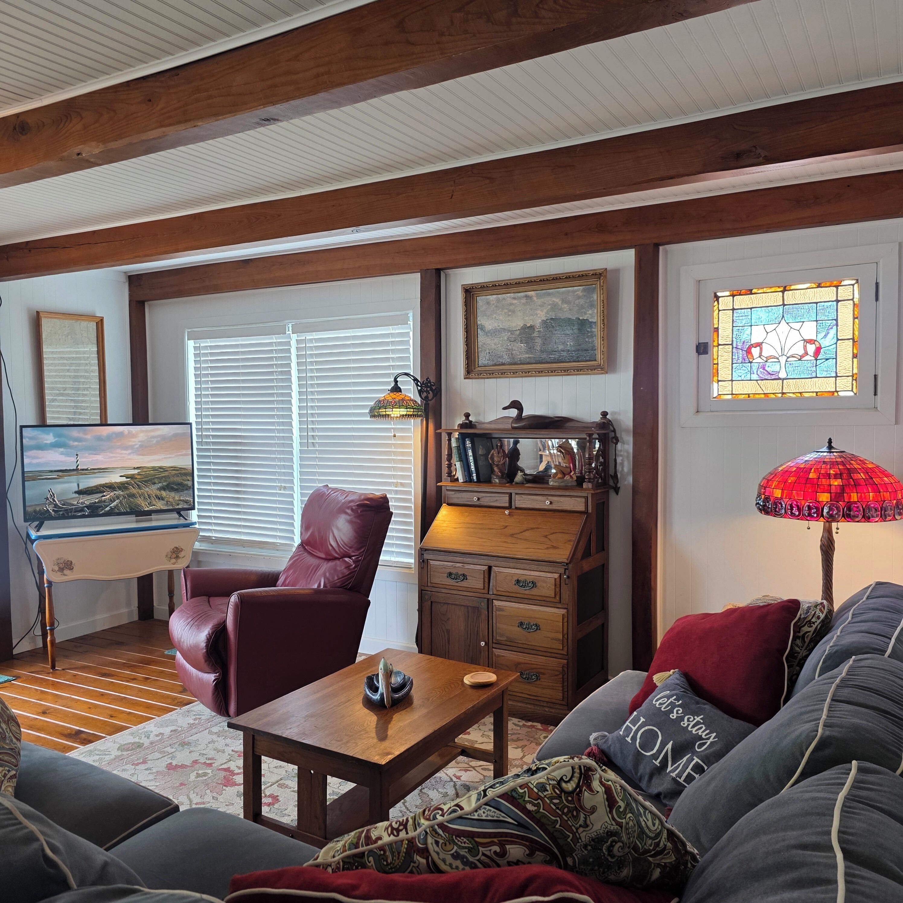 A cozy living room with a wooden desk, a leather chair, a sofa, and a red lamp.