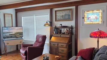 A cozy living room with a wooden desk, a leather chair, a sofa, and a red lamp.