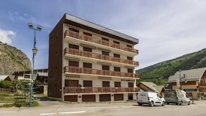 A multi-story hotel with balconies, a parking area, and a mountainous backdrop. - 300m from ski slopes, 2nd floor, balcony, parking, tv, ski locker, 22m², Valloire (Valloire)