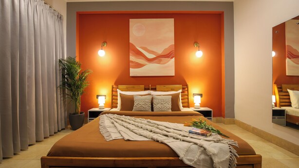 A bedroom with a large bed, two bedside tables, a nightstand, a potted plant, and a painting on the wall. - BedChambers Serviced Apartments SushantLok (Gurugram)