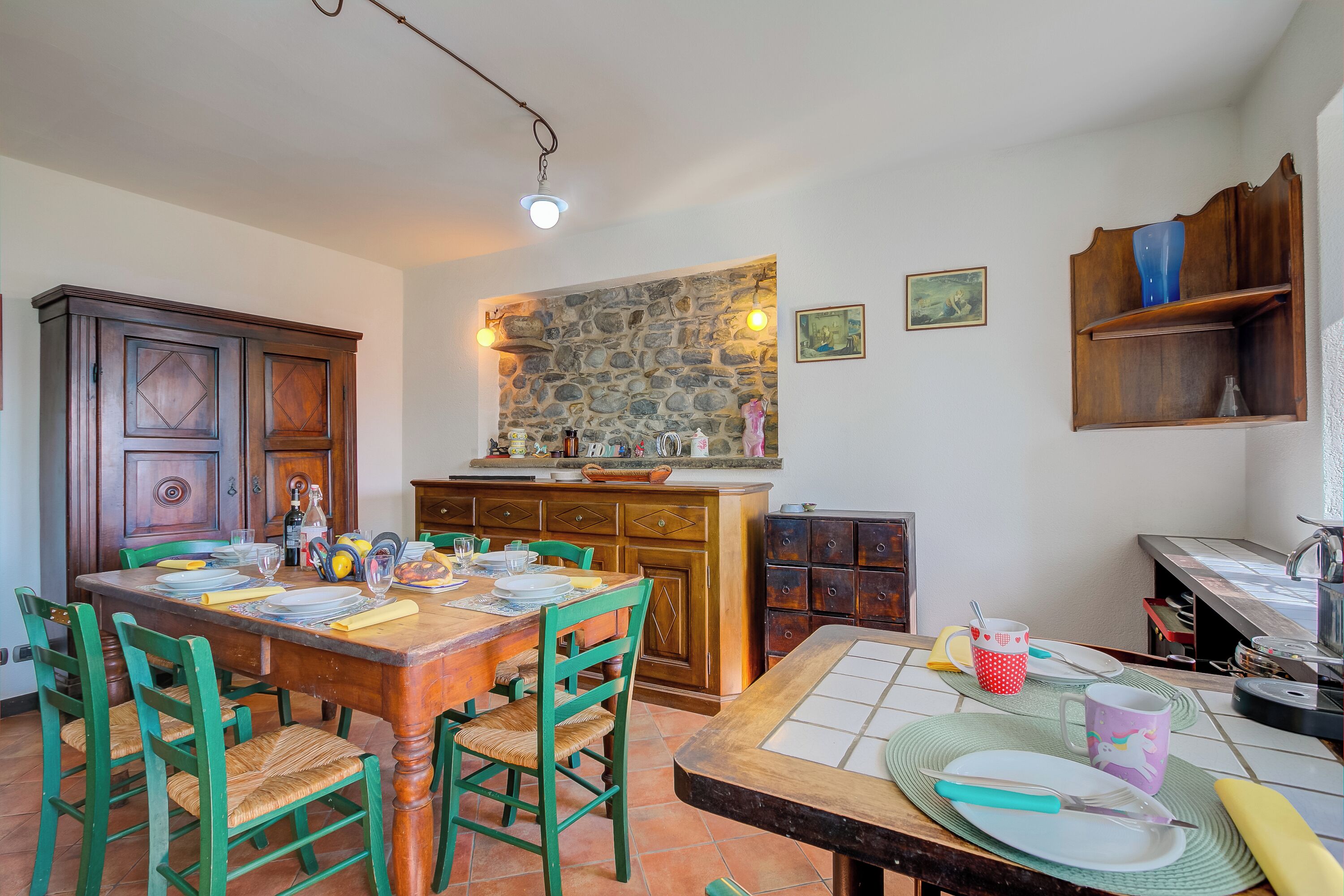 A dining area with a wooden table, green chairs, and a stone wall above.