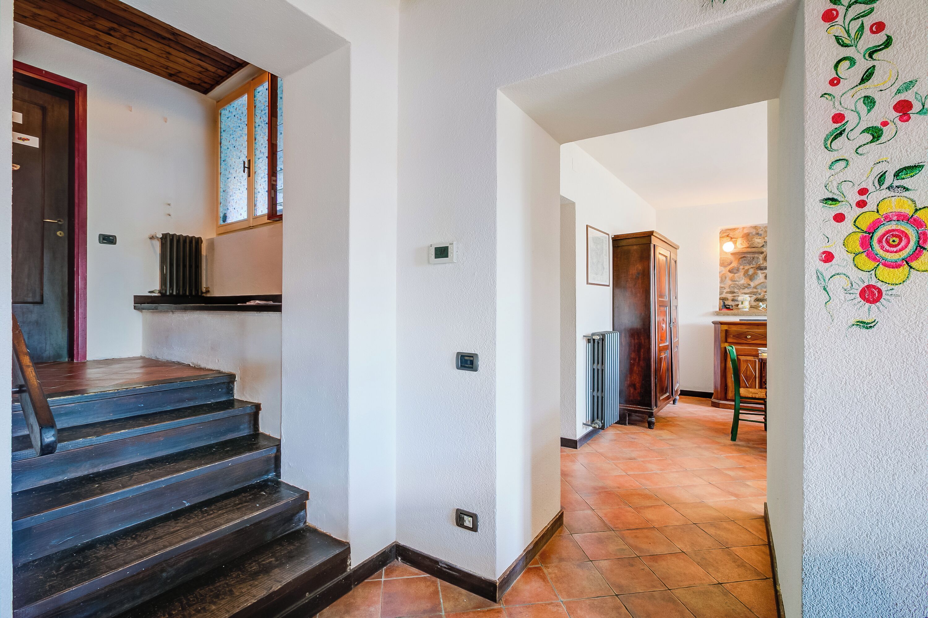 A staircase leading to a room with a wooden door, a radiator, and a wall with a floral design.