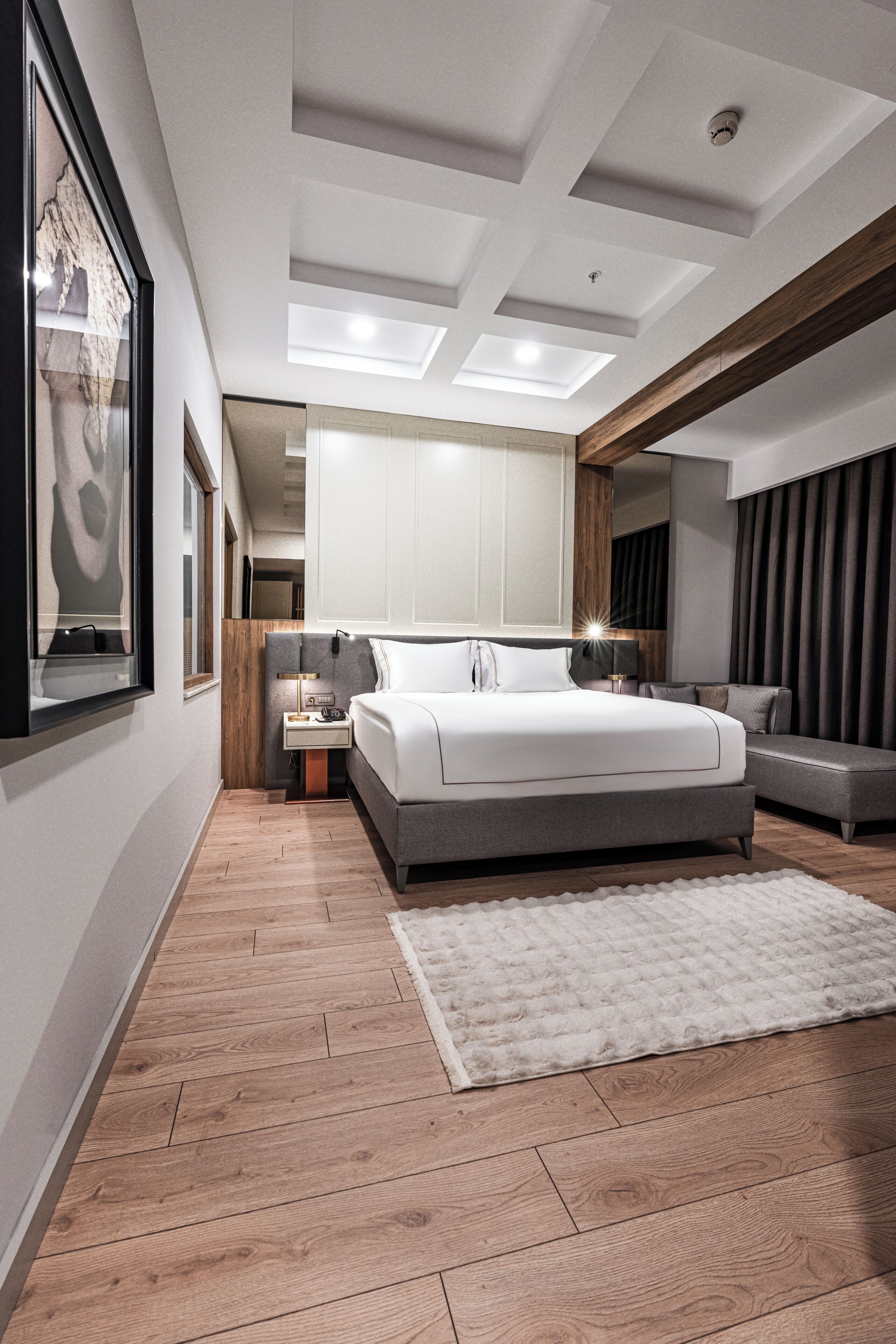 A modern bedroom with a large bed, a nightstand, a lamp, and a mirror.