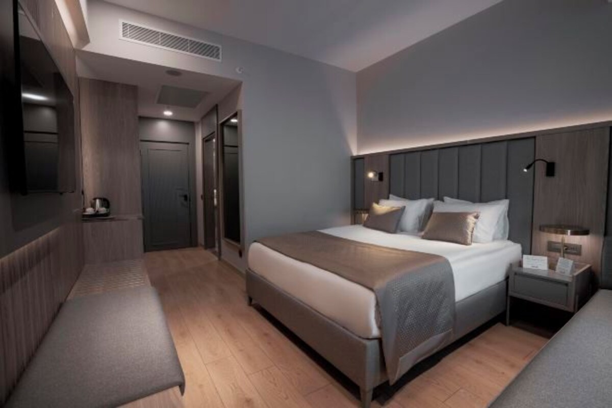 A modern hotel room with a large bed, bedside tables, a bench, and a TV.
