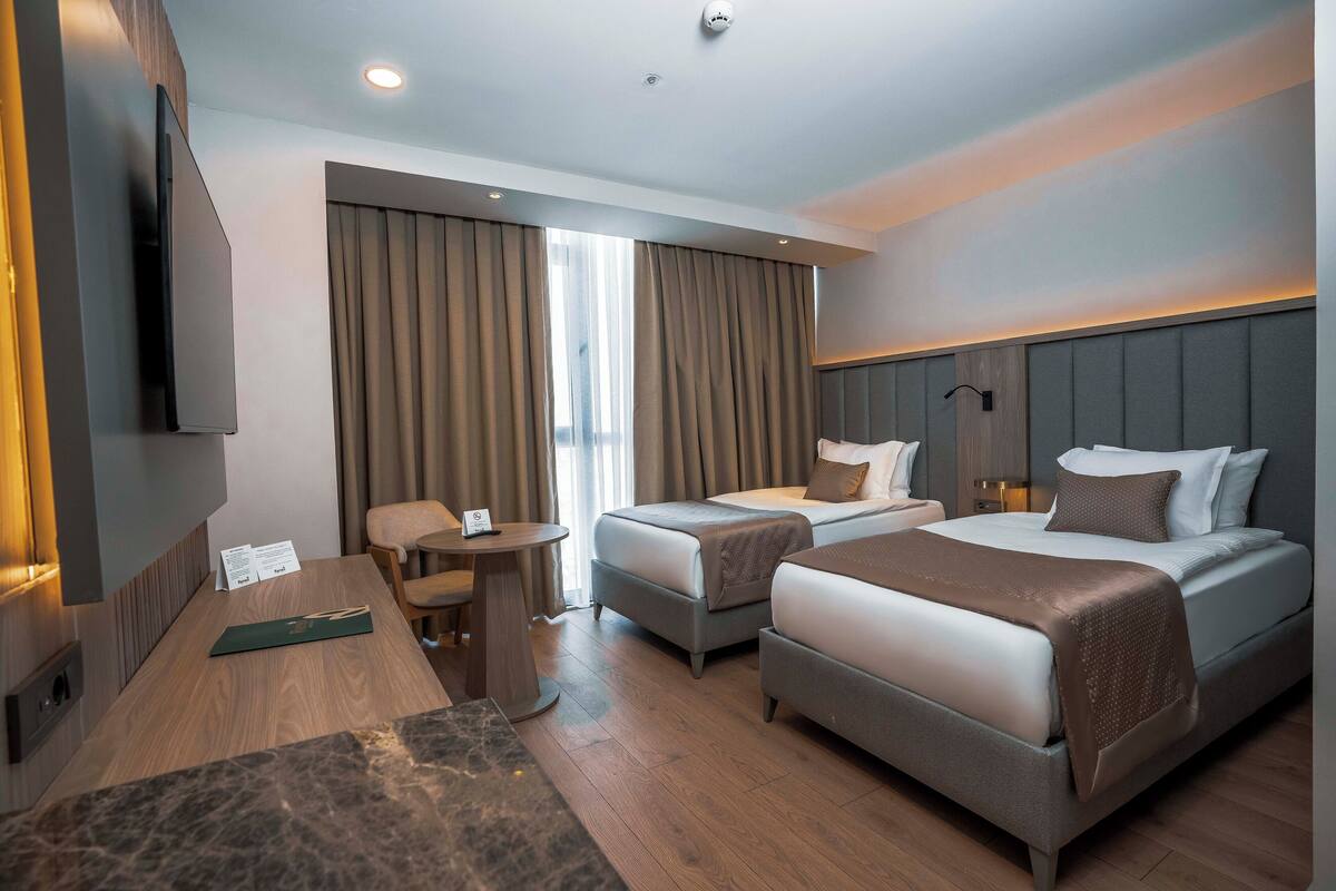 A hotel room with two beds, a desk, a chair, a TV, and a window with curtains.
