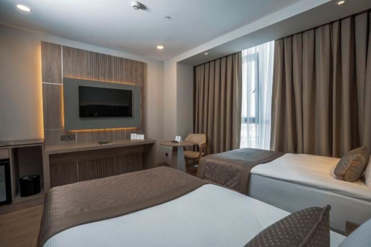A hotel room with two beds, a TV mounted on the wall, a desk, and a window with curtains.
