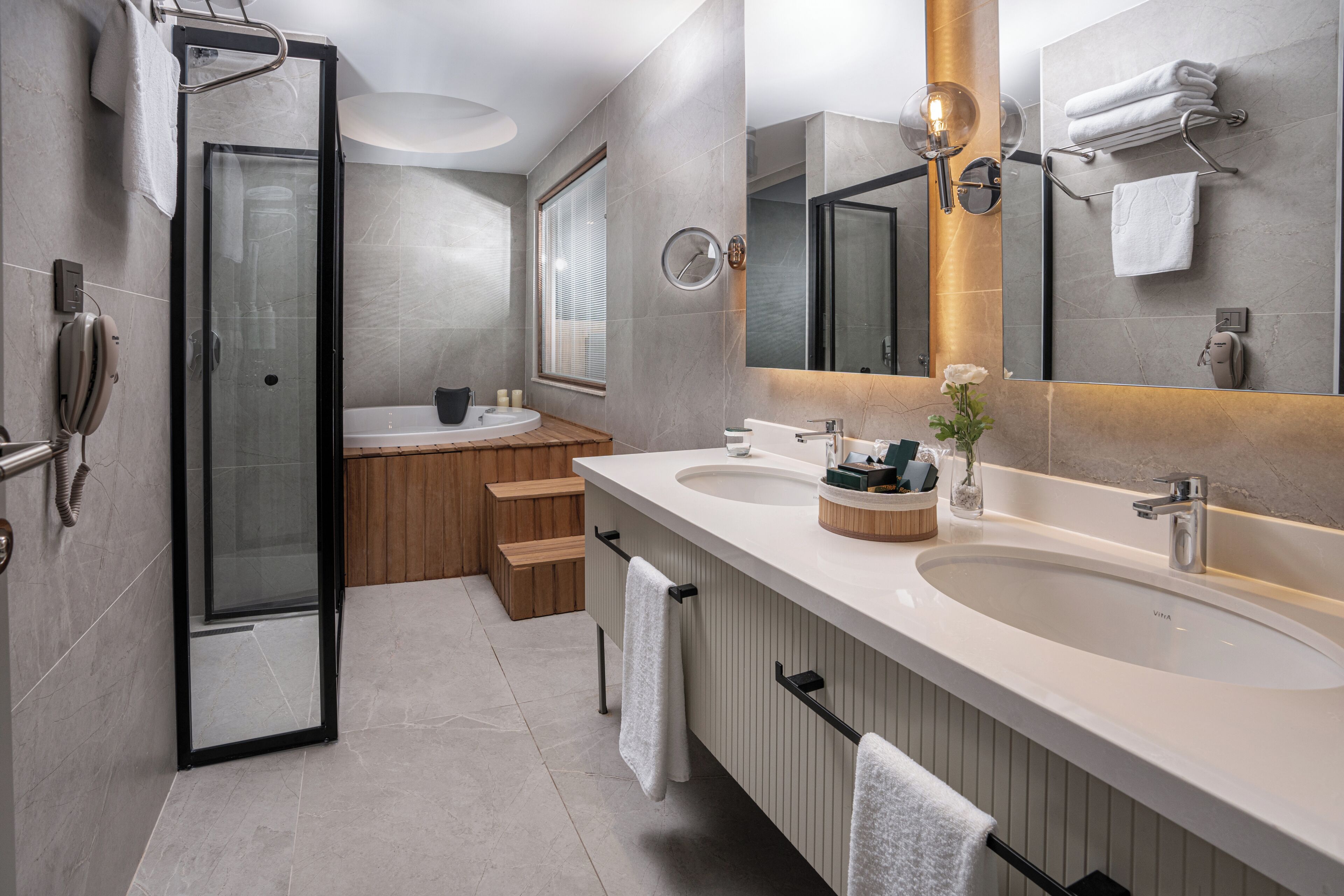 Ein modernes Badezimmer mit zwei Waschbecken, einer Duschkabine aus Glas, Holzsitzen und einem großen Spiegel.