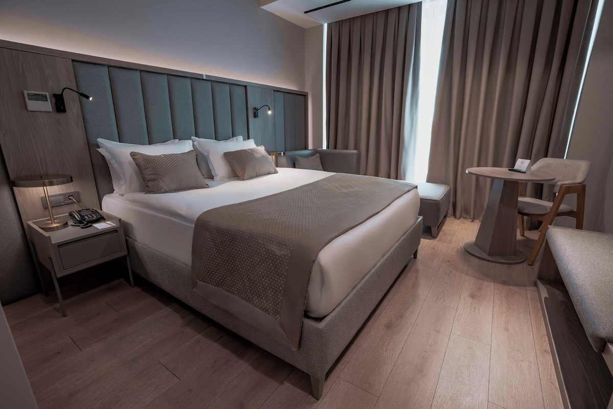 A modern hotel room with a large bed, bedside tables, a desk, and a chair.