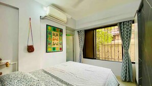 A bedroom with a bed, an air conditioning unit, a colorful wall decoration, and a window with curtains. - Charming 3 Bed 2 Bath in Bandra West with Balcony
 (Mumbai)