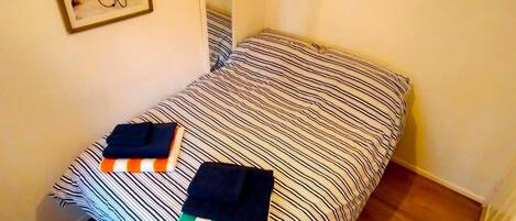 A small, single-bed room with a striped bedspread and two neatly folded towels.