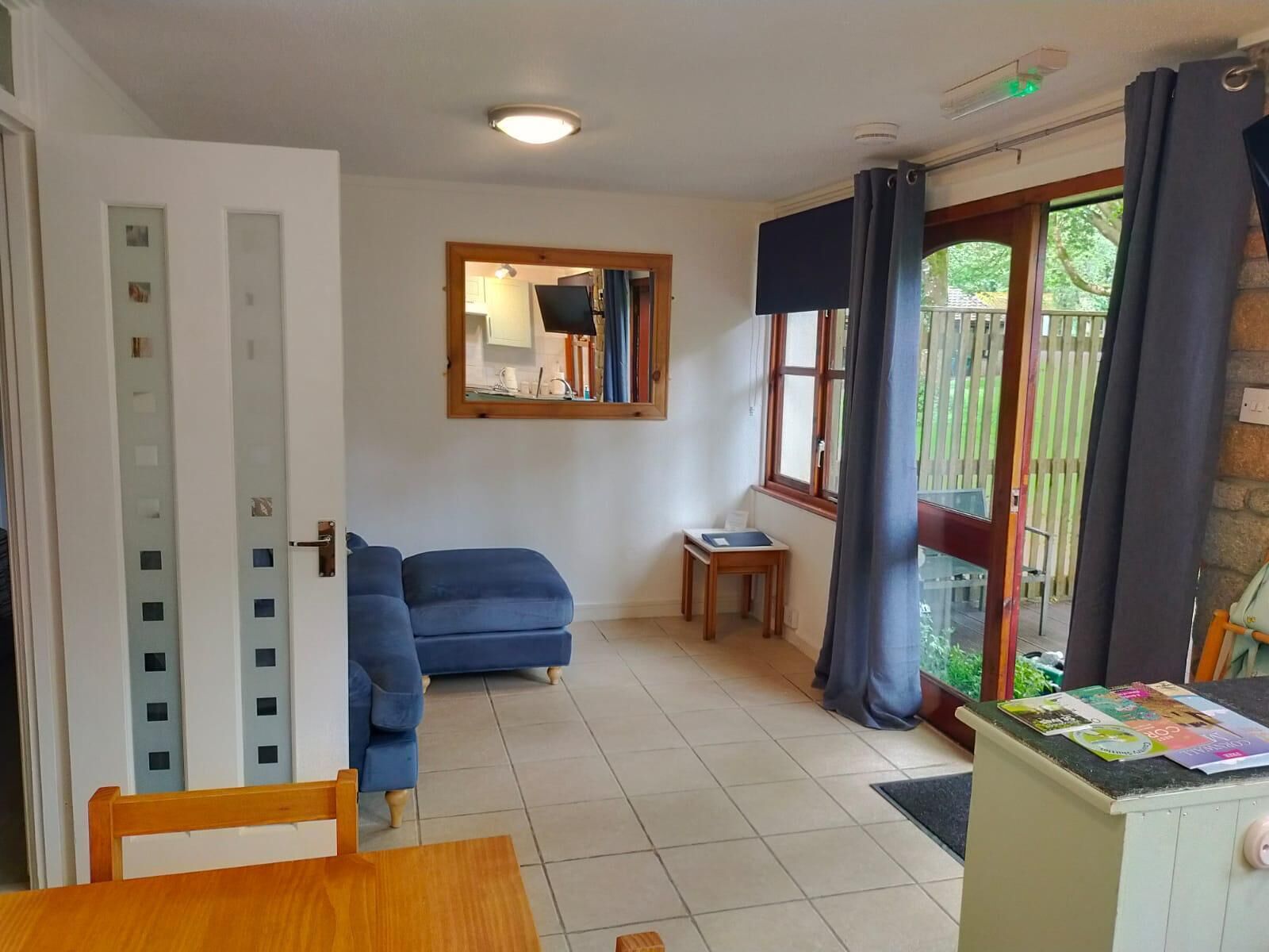 Ein Zimmer mit einem blauen Sofa, einem kleinen Holztisch, einem Spiegel und einem Fenster mit Vorhängen.
