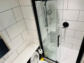 A modern bathroom with a glass-enclosed shower, white tiled walls, a toilet, and a sink.