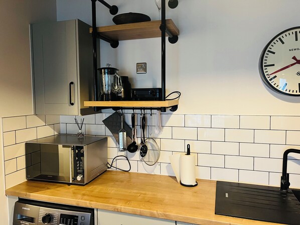 A kitchen with a built-in microwave, a toaster, a sink, and a clock on the wall.