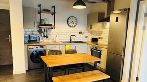 Una cucina compatta con un tavolo di legno, una lavatrice e un frigorifero in acciaio inossidabile.