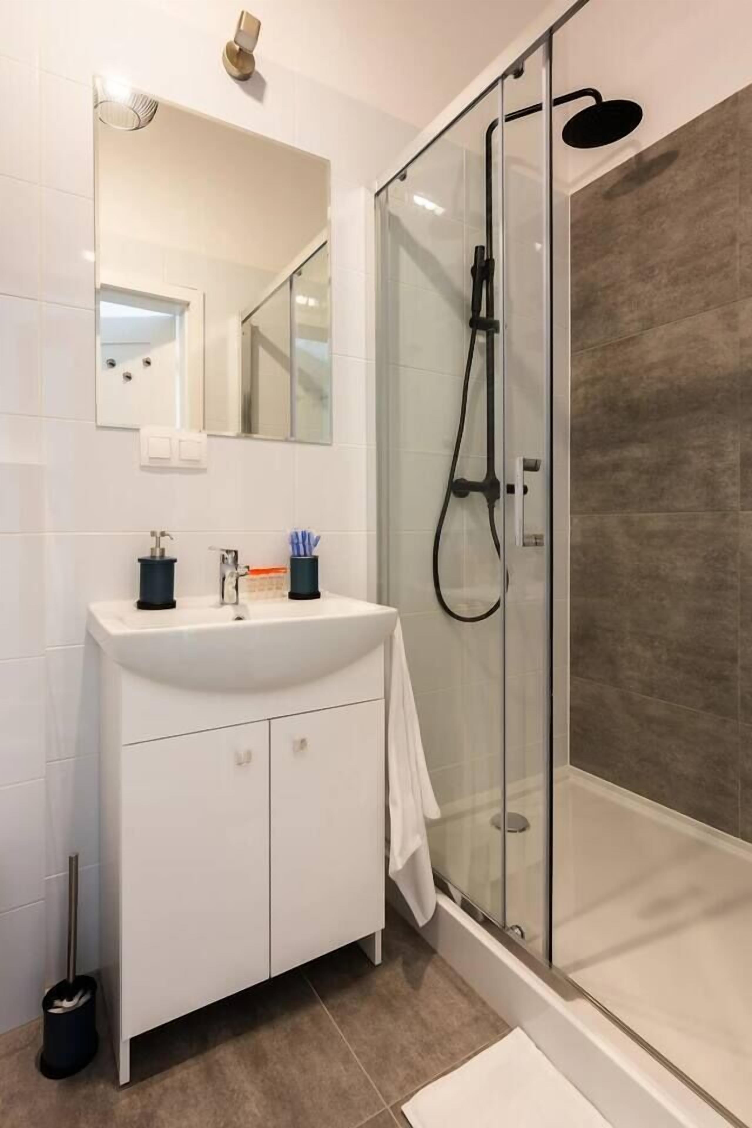 Une salle de bain moderne avec une douche à parois de verre, un meuble-lavabo blanc avec un miroir et un sol carrelé.